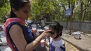 <p>Seorang perempuan mengenakan kacamata hitam untuk anaknya pada hari yang panas di New Delhi, India, Sabtu, 14 Mei 2022. Suhu di New Delhi mencapai 45 Derajat Celcius. (AP Photo/Manish Swarup)</p>