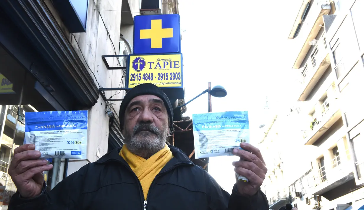 Seorang pria menunjukkan dua kemasan ganja yang baru dibeli di apotek di Montevideo, Uruguay (19/7). Uruguay menjadi yang pertama di dunia yang secara resmi melegalkan produksi dan penjualan ganja. (AFP Photo/Miguel Rojo)