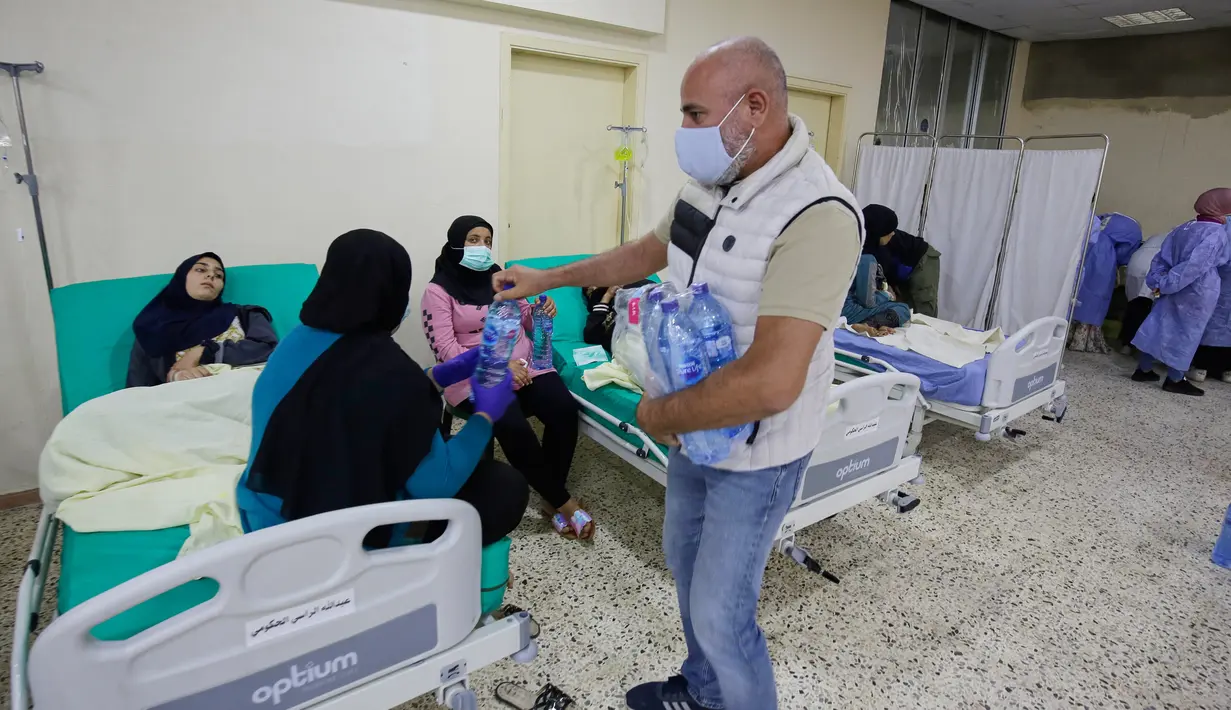 Seorang pria membagikan botol air kepada orang-orang yang menunggu pasien yang terinfeksi wabah kolera Vibrio, menerima perawatan di aula masjid yang diubah menjadi rumah sakit lapangan di Kota Bebnine, Distrik Akkar, Lebanon Utara, Rabu (26/10/2022). Kolera dapat menyebar dengan cepat, tergantung pada frekuensi paparan, populasi yang terpapar. (AFP/Ibrahim Chalhoub)