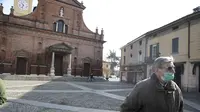 Seorang pria mengenakan masker berjalan di depan gereja San Biagio, Codogno, dekat Lodi, Italia Utara  (22/2/2020). Pihak berwenang Italia memerintahkan penutupan sekolah, bar, dan ruang publik lainnya di 12 kota, menyusul banyaknya kasus virus corona baru muncul di negara itu. (AP Photo/Luca Bruno)