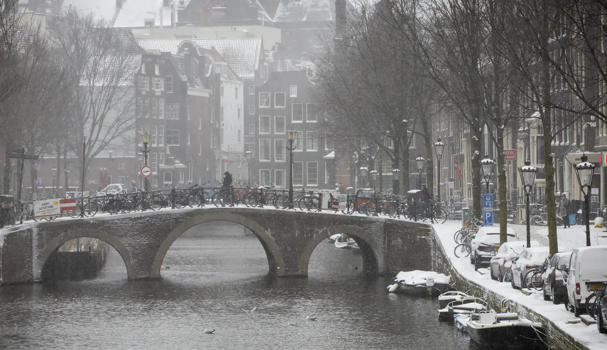 Seorang pria melintasi jembatan di Distrik Lampu Merah yang hampir kosong di Amsterdam, saat salju dan angin kencang menyelimuti sebagian besar wilayah Belanda, Minggu (7/2/2021). Peringatan bahaya cuaca ekstrem telah dikeluarkan oleh pihak BMKG Belanda. (AP Photo/Peter Dejong)