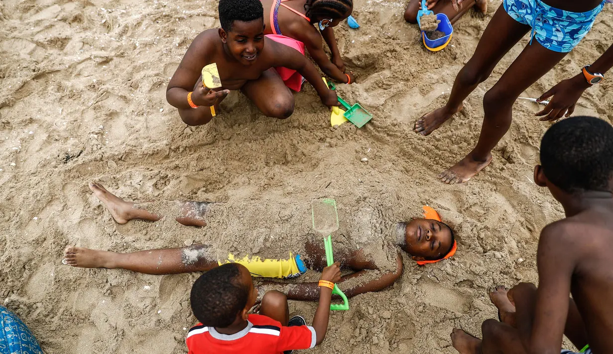 Anak-anak mengubur teman mereka di pasir saat mereka bermain di pantai Cabourg, barat laut (18/8/2021). Acara ini sebagai bagian dari kampanye "Lupa Liburan" yang diselenggarakan oleh LSM Prancis Secours Populaire untuk anak-anak yang keluarganya tidak mampu pergi berlibur. (AFP/Sameer Al-Doumy)