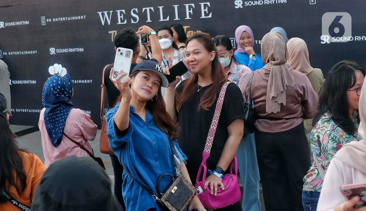Penggemar Westlife berswafoto saat tiba untuk menonton konser bertajuk 'The Wild Dreams Tour 2023' di kawasan Stadion Utama Gelora Bung Karno Sabtu (11/2/2023). Penampilan Westlife menjadi penantian penggemar yang datang dari berbagai daerah. Bahkan, sebagian penggemar juga datang dari sejumlah kota di luar Jabodetabek. (Liputan6.com/Angga Yuniar)
