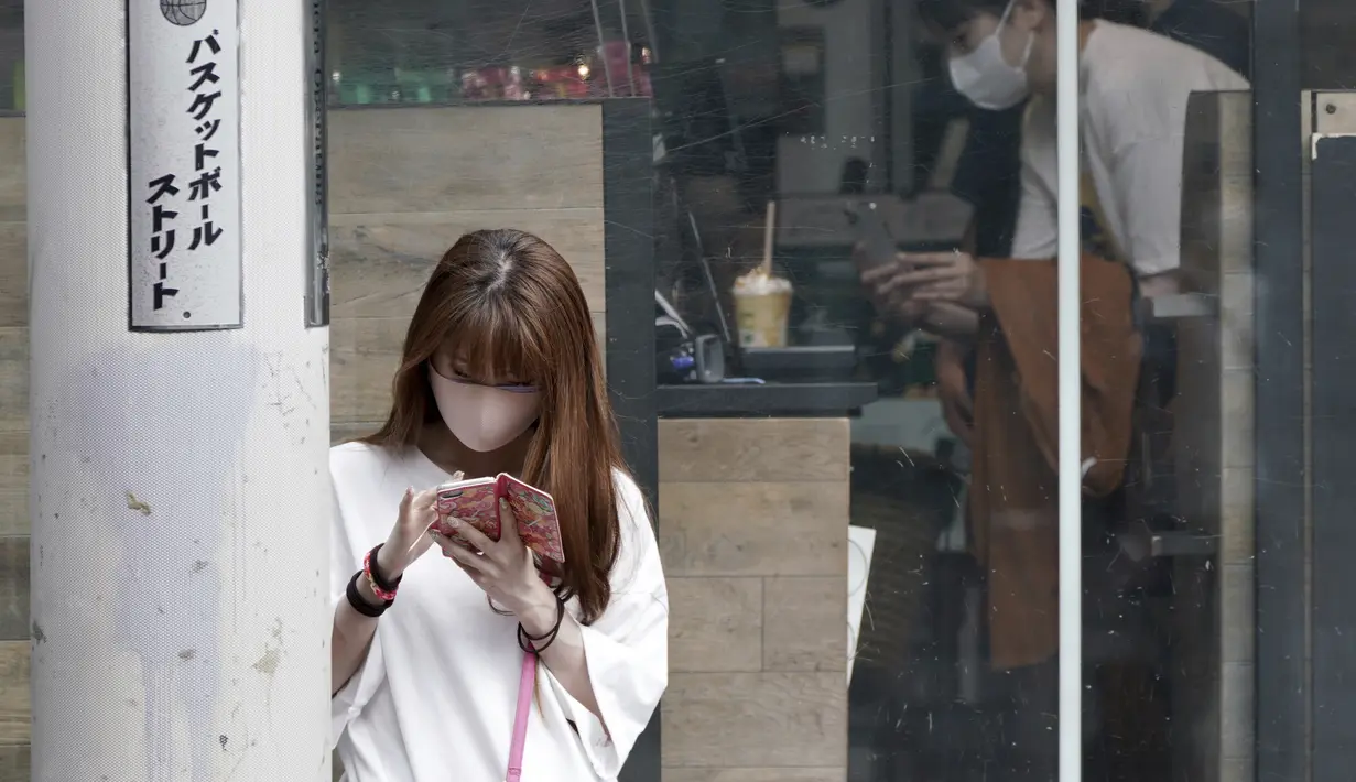 Seorang perempuan mengenakan masker melihat ponsel di distrik Shibuya, Tokyo, Kamis (30/9/2021). Jepang akan mencabut keadaan darurat COVID-19 di semua wilayah pada akhir September. (AP Photo/Eugene Hoshiko)