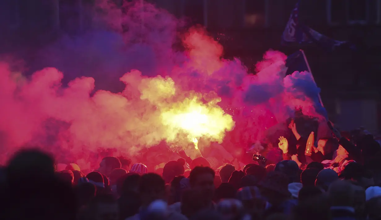 Para fans Glasgow Rangers menyalakan granat asap di George Square, pusat kota Glasgow (7/3/2021) untuk merayakan keberhasilan tim kesayangan mereka merebut gelar Liga Utama Skotlandia setelah memimpin 20 poin dari saingan terdekat, Glasgow Celtic. (AFP/Andy Buchanan)