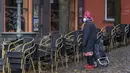 Seorang wanita mengenakan masker saat melewati teras kosong di kawasan Marrolles di Brussels, Rabu (17/11/2021). Pemerintah Belgia mewajibkan kembali penggunaan masker dan memberlakukan warga bekerja dari rumah dalam upaya untuk menahan lonjakan baru kasus COVID-19. (AP Photo/Olivier Matthys)