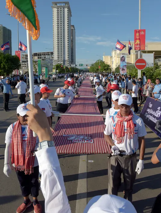Warga Kamboja membentangkan syal krama sepanjang 1.149,8 meter untuk memecahkan rekor Guinness di Phnom Penh, Minggu (1/7). Syal krama di Kamboja memecahkan rekor sebagai syal tenun terpanjang di dunia. (AFP/TANG CHHIN Sothy)