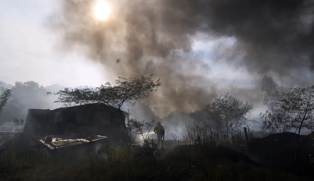 Petugas pemadam kebakaran menyiram gubuk untuk mencegahnya terbakar selama kebakaran semak di lingkungan Banco San Miguel di Asuncion, Paraguay (18/1/2022). Cuaca kering yang tidak biasa memicu kebakaran di lapangan terbuka, peternakan pribadi, dan lahan publik sekitar kota. (AP Photo/Jorge Saenz)