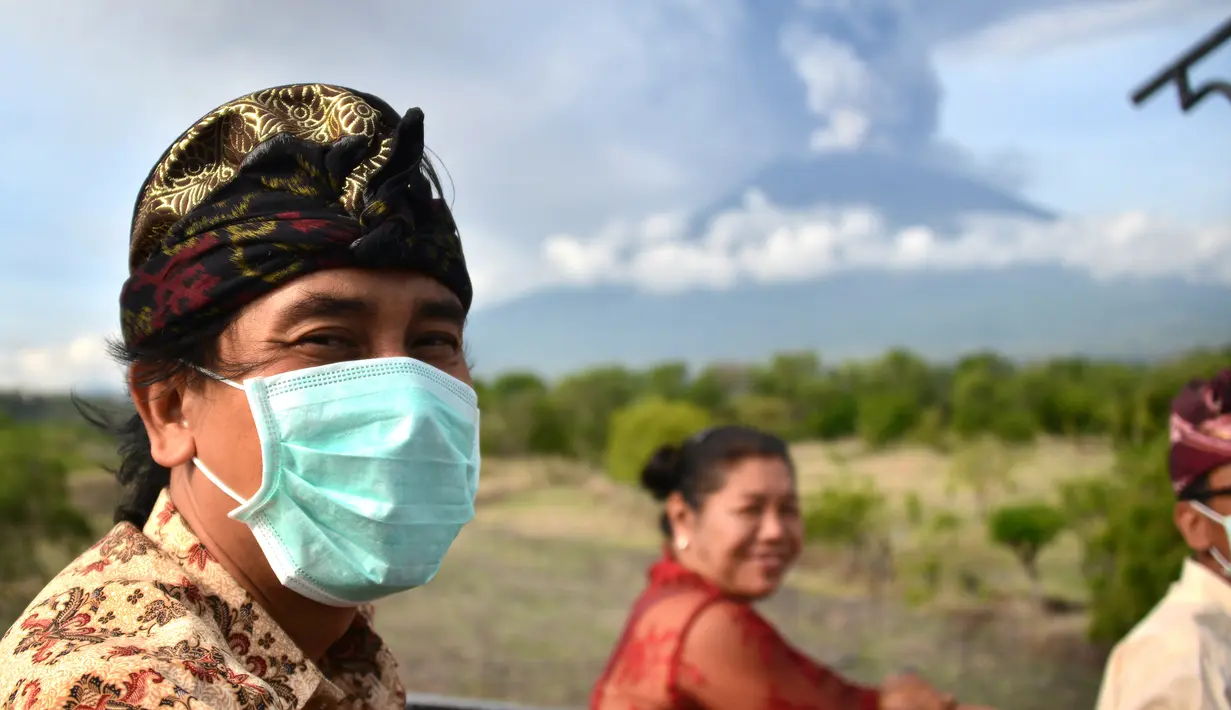 Seorang pria mengenakan masker saat menaiki mobil bak terbuka melewati Gunung Agung di Kabupaten Karangasem, Bali (27/11). Sebelumnya, Gunung Agung telah mengalami erupsi sejak Sabtu (25/11) sore.  (AFP/Sonny Tumbelaka)