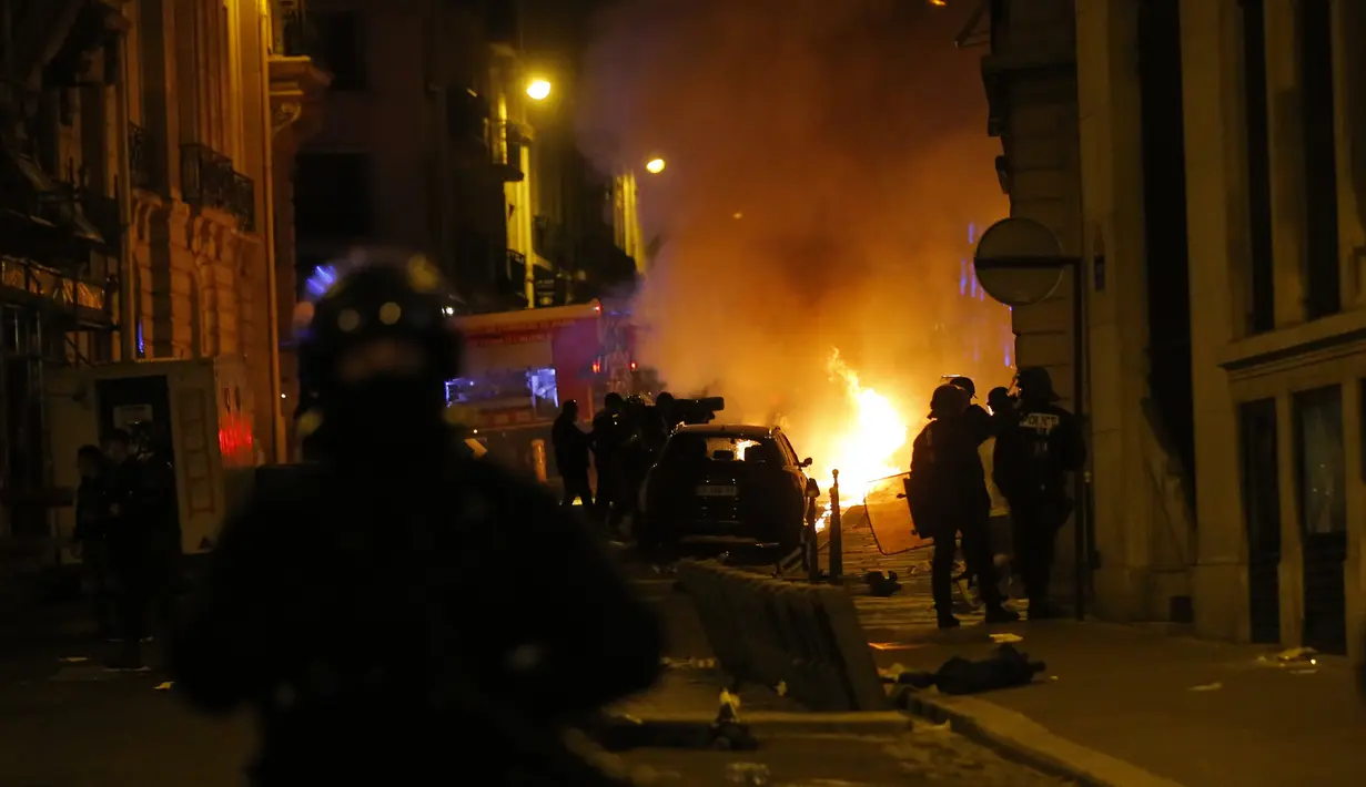 Petugas polisi Prancis menyaksikan sebuah mobil terbakar saat bentrok dengan suporter PSG di dekat jalan Champs-Elysee setelah Munchen yang dimainkan di Lisbon, Portugal di Paris, Minggu (23/8/2020) Munchen menang 1-0 atas PSG. (AP Photo/Michel