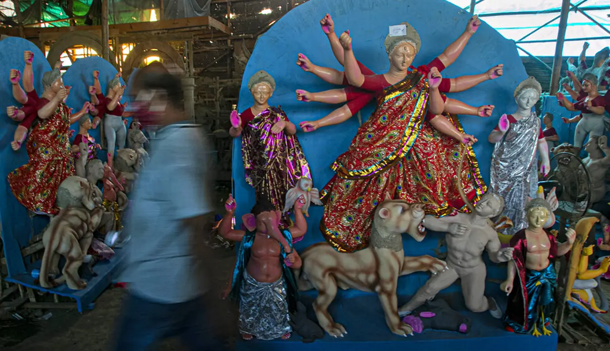 Seniman berjalan melewati patung Dewi Durga jelang Festival Durga Puja di Gauhati, India, Jumat (16/10/2020). Para pejabat kesehatan memperingatkan tentang potensi penyebaran COVID-19 selama musim festival keagamaan dengan pertemuan besar di kuil dan distrik perbelanjaan. (AP Photo/Anupam Nath)