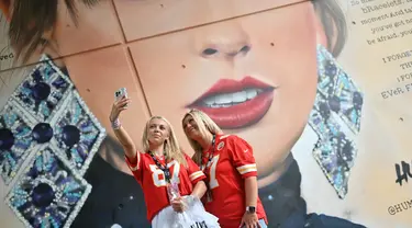 Penggemar Taylor Swift berswafoto dengan latar belakang mural sang penyanyi yang dibuat oleh seniman jalanan MurWalls, di luar Stadion Wembley, London, Kamis (15/8/2024). (JUSTIN TALLIS / AFP)