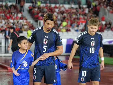 Pemain Jepang, Hidemasa Morita (kedua kiri) menuntun anak kecil yang ditugaskan sebagai player escort dalam pertandingan lanjutan putaran ketiga Grup C Kualifikasi Piala Dunia 2026 melawan Timnas Indonesia di Stadion Utama Gelora Bung Karno (SUGBK), Senayan, Jakarta, Jumat (15/11/2024). (Bola.com/Bagaskara Lazuardi)