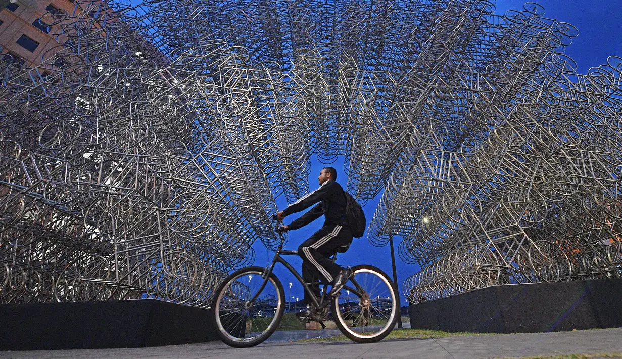 Seorang pria mengendarai sepeda melewati instalasi seni seniman China Ai Weiwei yang berjudul 'Forever Cycles' di Rio de Janeiro, Brasil, Senin (19/8/2019). Instalasi ini terdiri lebih dari 1.000 sepeda stainless steel. (CARL DE SOUZA/AFP)