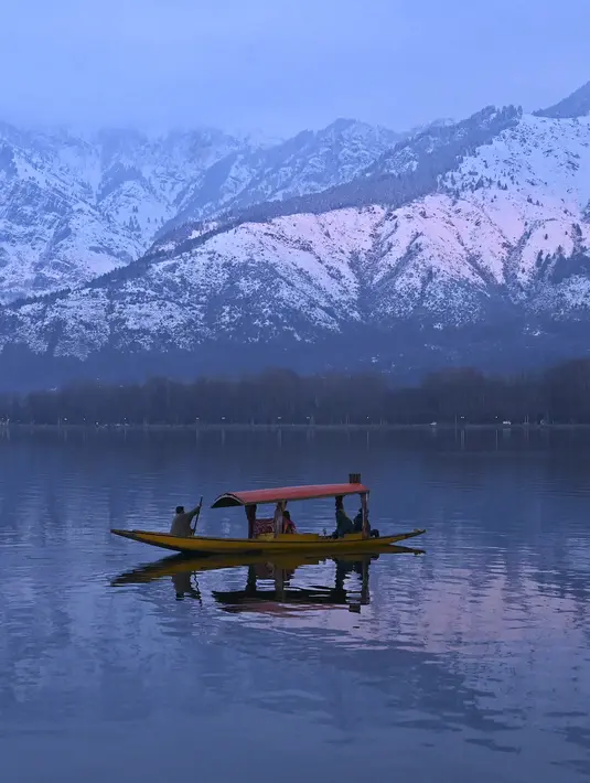 Orang-orang menikmati perjalanan dengan perahu dengan latar belakang pegunungan yang tertutup salju di danau Dal di Srinagar (11/1/2022). Daya tarik keindahan yang sempurna membuat danau Dal dijuluki sebagai Jewel in the Crown of Kashmir atau Srinagar Jewel. (AFP/Tauseef Mustafa)