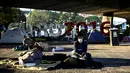 Seorang pencari suaka Afghanistan yang mengenakan masker duduk di atas selimut di kamp migran darurat yang terletak di bawah jembatan jalan raya A1 di utara pinggiran Kota Paris Saint-Denis di Prancis (16/9/2020). Mereka bertahan menunggu kepastian negara pemberi suaka. (AFP/Christophe Archambault)