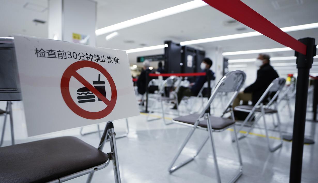 Kertas bertuliskan, "Tolong jangan makan atau minum 30 menit sebelum tes." terlihat saat para Penumpang duduk dan menunggu giliran selama proses karantina pencegahan virus corona setelah mendarat di Bandara Internasional Narita di Narita, timur Tokyo, Jepang (2/12/2021). (AP Photo/Hiro Komae)