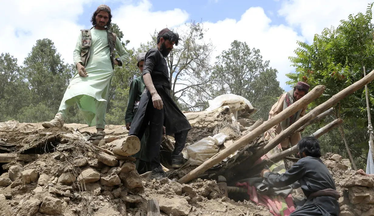 Penduduk desa mengumpulkan barang-barang dari bawah puing-puing sebuah rumah yang hancur akibat gempa bumi di Distrik Spera, bagian barat daya Provinsi Khost, Afghanistan, 22 Juni 2022. Gempa menewaskan lebih dari 1.000 orang dan melukai 1.500 lainnya. (AP Photo)
