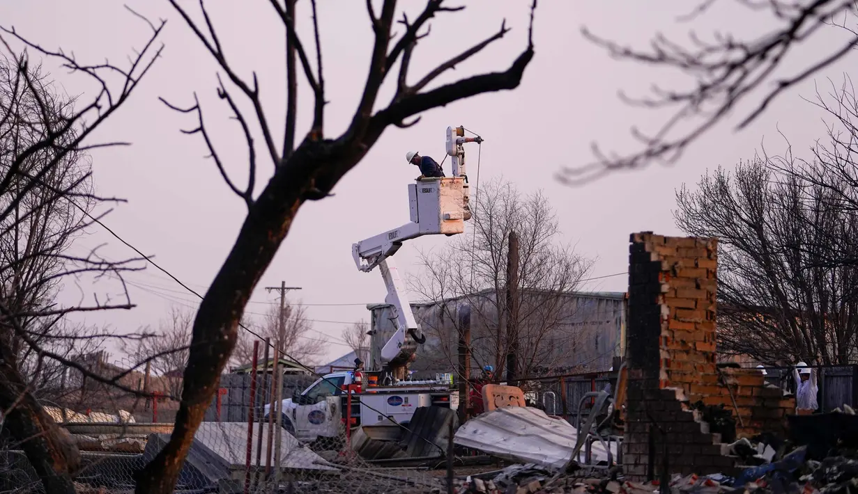 Para pekerja utilitas bekerja di atas kabel listrik yang tumbang di dekat perumahan yang terbakar oleh kebakaran Smokehouse Creek, Rabu, 28 Februari 2024, di Canadian, Texas. (AP Photo/Julio Cortez)