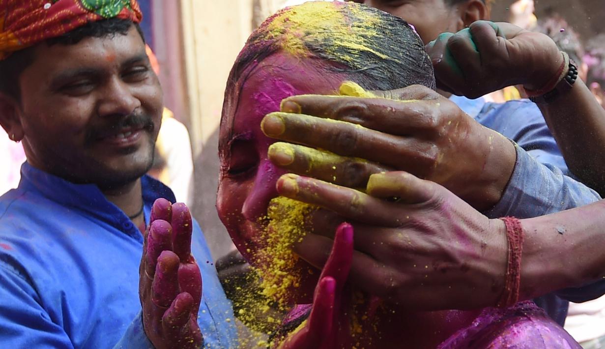 Sejumlah pria mengolesi bubuk warna pada wajah seorang gadis saat merayakan festival Holi di sebuah kuil di desa Nandgaon, Uttar Pradesh, 5 Maret 2020. Festival Holi diselenggarakan pada awal musim semi yaitu pada akhir Februari hingga Maret, tepatnya sesudah bulan purnama. (Money SHARMA/AFP)