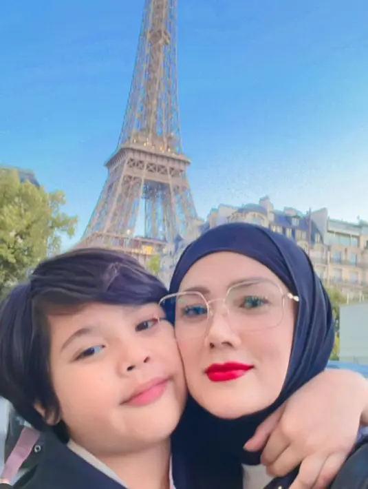 Mulan Jameela yang mengenakan kerudung hitam foro selfie bersama Ali di depan Menara Eiffel. Mulan pun tampil dengan makeup bright mengaplikasikan lipstik merah.  [@mulanjameela1]