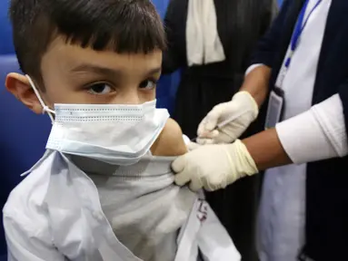 Petugas kesehatan menyuntikkan vaksin covid-19 Pfizer-BioNTech kepada seorang anak di pusat vaksinasi di Kuwait International Fairground di Kuwait City pada 3 Februari 2022. Kementerian kesehatan Kuwait mulai memvaksinasi anak usia 5 hingga 11 tahun. (YASSER AL-ZAYYAT / AFP)