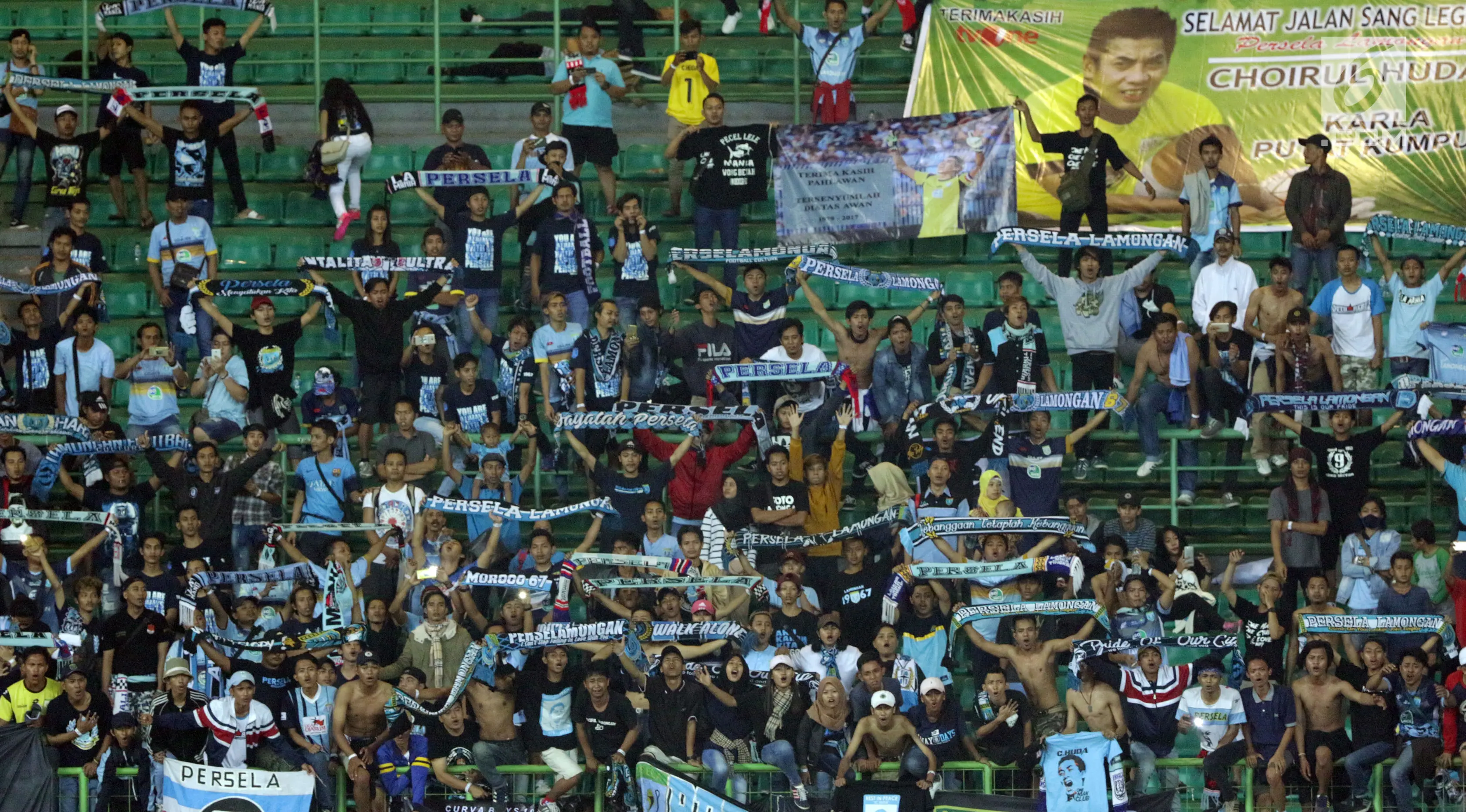 Suporter Laskar Joko Tingkir membentangkan syal dan poster bergambar alm Choirul Huda saat menyaksikan laga Persela melawan Bhayangkara FC di Stadion Patriot Candrabhaga, Bekasi, Jumat (27/10). (Liputan6.com/Helmi Fithriansyah)