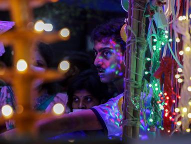 Cahaya dari barang-barang dekoratif jatuh di wajah pelanggan di kios pinggir jalan menjelang Diwali, festival lampu Hindu, di Kolkata, India, Rabu (27/10/2021). Diwali adalah salah satu festival paling penting dalam agama Hindu, yang didedikasikan untuk ibadah Dewi Laksmi. (AP Photo/Bikas Das)