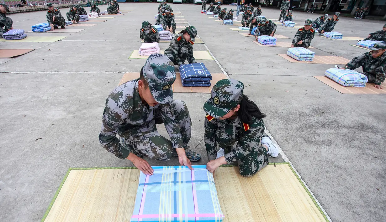 Tentara (kiri) mengajari mahasiswa baru melipat selimut selama sesi pelatihan militer di sebuah kampus di Yangzhou, Jiangsu, China, Jumat (6/9/2019). China memilih pelatihan militer atau dikenal dengan istilah 'Junxun' sebagai program orientasi mahasiswa baru. (STR/AFP)