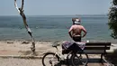 Seorang pria berdiri di sepanjang pantai menyaksikan orang-orang mandi di Thessaloniki, Yunani utara (23/6/2021).  Yunani bersiap menghadapi gelombang panas pertama musim panas, mendorong suhu siang hari ke wilayah 40+ Celcius di banyak bagian negara. (AFP/ Sakis Mitrolidis)