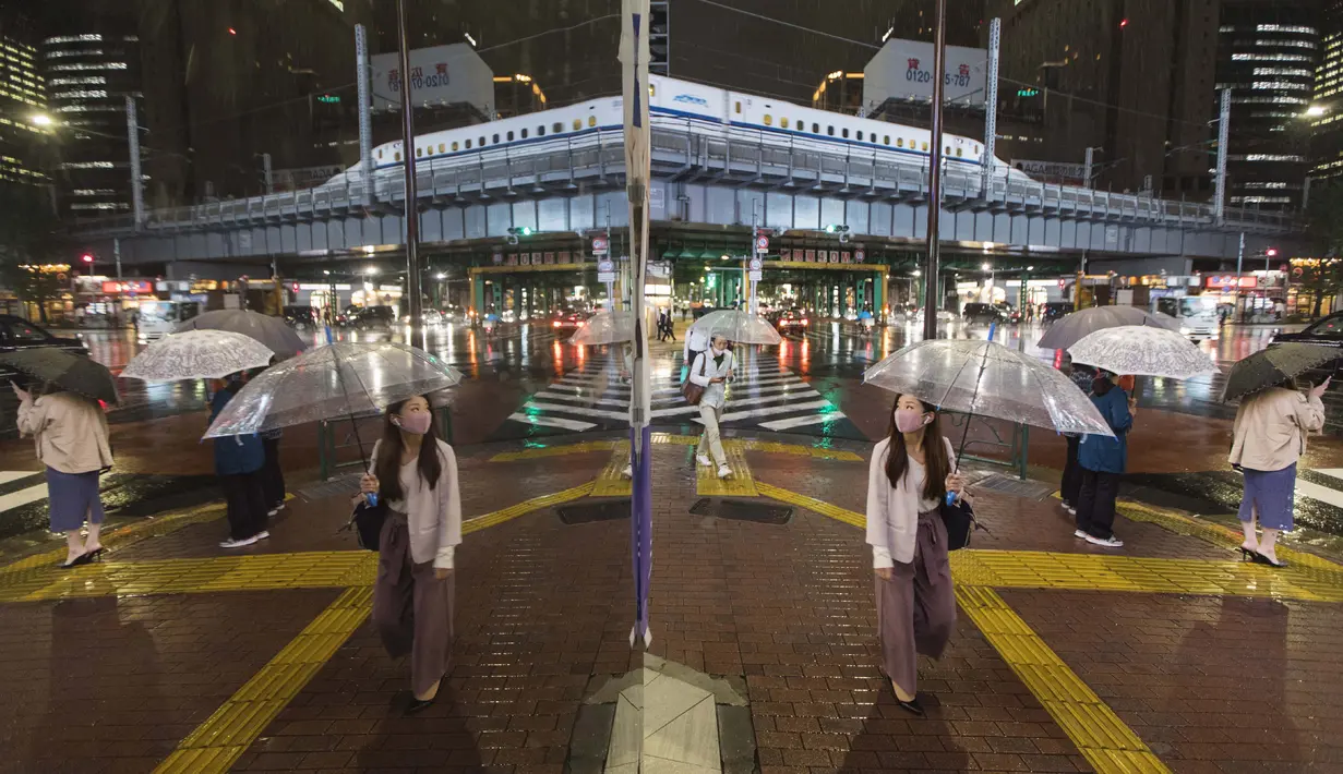Orang-orang yang terlihat dalam refleksi berjalan melintasi persimpangan di tengah hujan di Tokyo pada hari Kamis (8/10/2020). (AP Photo/Hiro Komae)