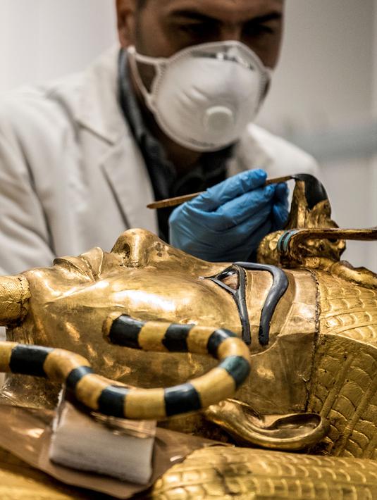 Arkeolog merestorasi sarkofagus atau peti mati emas Firaun Tutankhamun di laboratorium restorasi Grand Egyptian Museum (GEM), Giza, Mesir, Senin (13/4/2020). Firaun Tutankhamun merupakan Raja Mesir Kuno yang memerintah antara tahun 1342-1325 SM. (Khaled DESOUKI AFP)