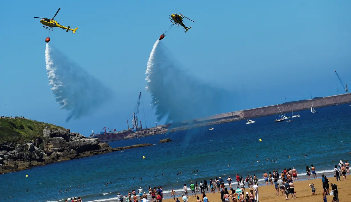 Aksi tim aerobatik Patrulla Aspa saat bermanuver mengeluarkan air saat menghebohkan pengunjung di atas Pantai San Lorenzo di Gijon, Spanyol, Minggu (24/7). (REUTERS/Eloy Alonso)