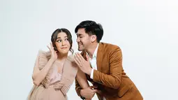 Dampingi sang istri jalani pemotretan, Kevin Aprilio mengenakan setelan jas kotak-kotak warna cokelat yang kontras dengan sang istri. Berpose seperti berbisik dan menggandeng sang istri, pasangan yang terpaut usia 1 tahun ini bak ABG. Kevin berpose seperti berbisik, sementara Vicy Melanie berpose seakan mendengarkan bisikan dari sang suami dengan ekspresi penasaran. (Liputan6.com/IG/@vicymelanie)