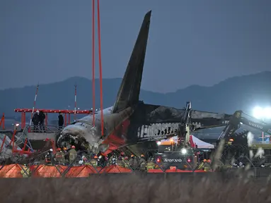 Petugas pemadam kebakaran dan penyelamat masih terus bekerja di dekat lokasi pesawat Jeju Air berjenis Boeing 737-800 yang jatuh dan terbakar di Bandara Internasional Muan, Provinsi Jeolla Selatan, sekitar 288 kilometer sebelah barat daya Seoul, Korea Selatan pada Minggu 29 Desember 2024. (JUNG YEON-JE/AFP)