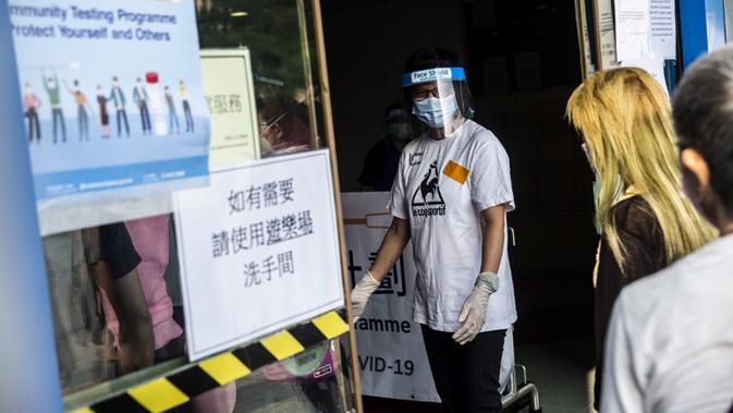 Petugas (kiri) memberi isyarat kepada orang-orang yang menunggu dalam antrean di pusat pengujian virus corona COVID-19, Hong Kong, Selasa (1/9/2020). Hong Kong mulai melakukan tes massal virus corona COVID-19. (ISAAC LAWRENCE/AFP)