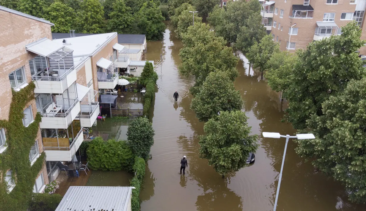 orang-orang melintasi daerah banjir setelah hujan lebat di Hemsta, Gavle, Swedia Rabu (18/8/2021). Hujan deras di Swedia timur telah menggenangi beberapa area pemukiman, dengan beberapa jalan dan jembatan tergenang saat hujan terus turun. (Fredrik Sandberg/TT News Agency/AFP)