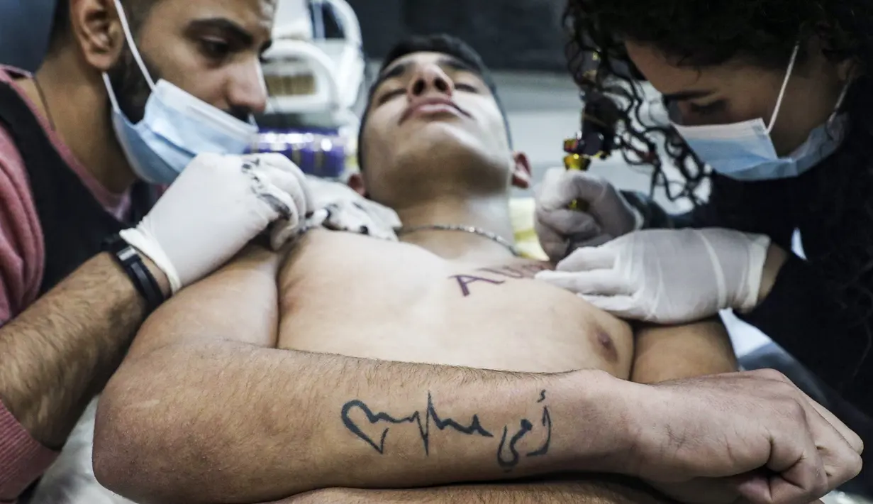Naim Abdallah dibantu oleh seorang asisten saat menuangkan kreasinya di atas tubuh klien di ruang kerjanya di Kota Betlehem di Tepi Barat (24/1/2021). (AFP/Hazem Bader)