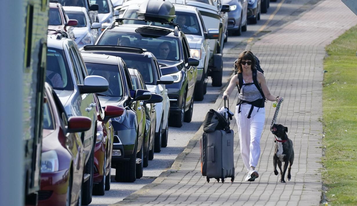 Terri Mills berjalan dengan anjingnya, Carlos, melewati barisan kendaraan yang menunggu untuk memasuki Kanada di perbatasan Peace Arch, Blaine, Washington, Senin (9/8/2021). Kanada mencabut larangan terhadap warga AS melintasi perbatasan negaranya. (AP Photo/Elaine Thompson)