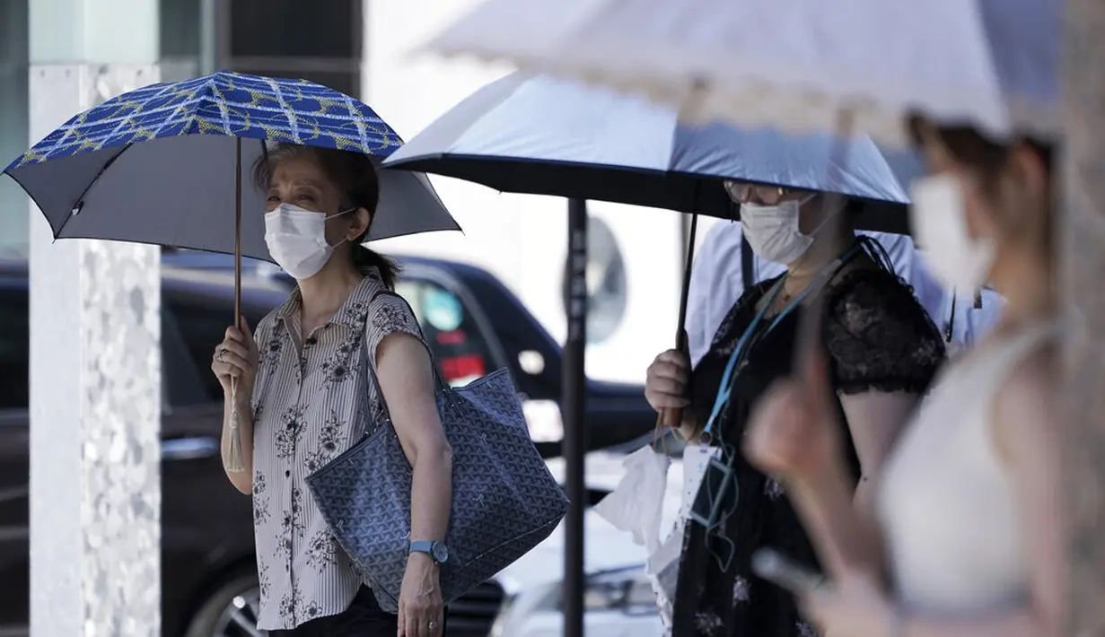 Warga mengenakan masker untuk mencegah penyebaran Covid-19 menggunakan payung di bawah sinar matahari di Tokyo (12/8/2020). Menurut Badan Meteorologi Jepang, cuaca panas telah ditetapkan dengan suhu naik lebih dari 34 derajat Celcius (93,2 derajat Fahrenheit) di Tokyo. (AP Photo/Eugene Hoshiko)