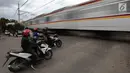 Pengendara sepeda motor menghentikan kendaraannya saat sebuah kereta api melintas di perlintasan kereta api tanpa palang pintu di kawasan Kelingkit, Rawa Buaya, Jakarta Barat, Selasa (26/2). (Liputan6.com/Johan Tallo)