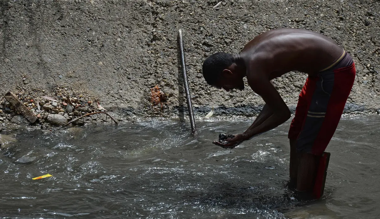 Seorang pria mengeluarkan lumpur dari dasar saluran pembuangan saat dia mencari logam berharga di Sungai Guaire, di Caracas, Venezuela (1/2). Puluhan warga mencari logam atau tembaga setiap hari di Sungai Guaire. (AFP Photo/Federico Parra)