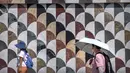 Orang-orang menggunakan topi matahari dan payung untuk melindungi diri dari sinar matahari saat mereka berjalan di luar pusat perbelanjaan pada hari yang panas di luar musimnya di Beijing, Sabtu, 24 Juni 2023. (AP Photo/Mark Schiefelbein)