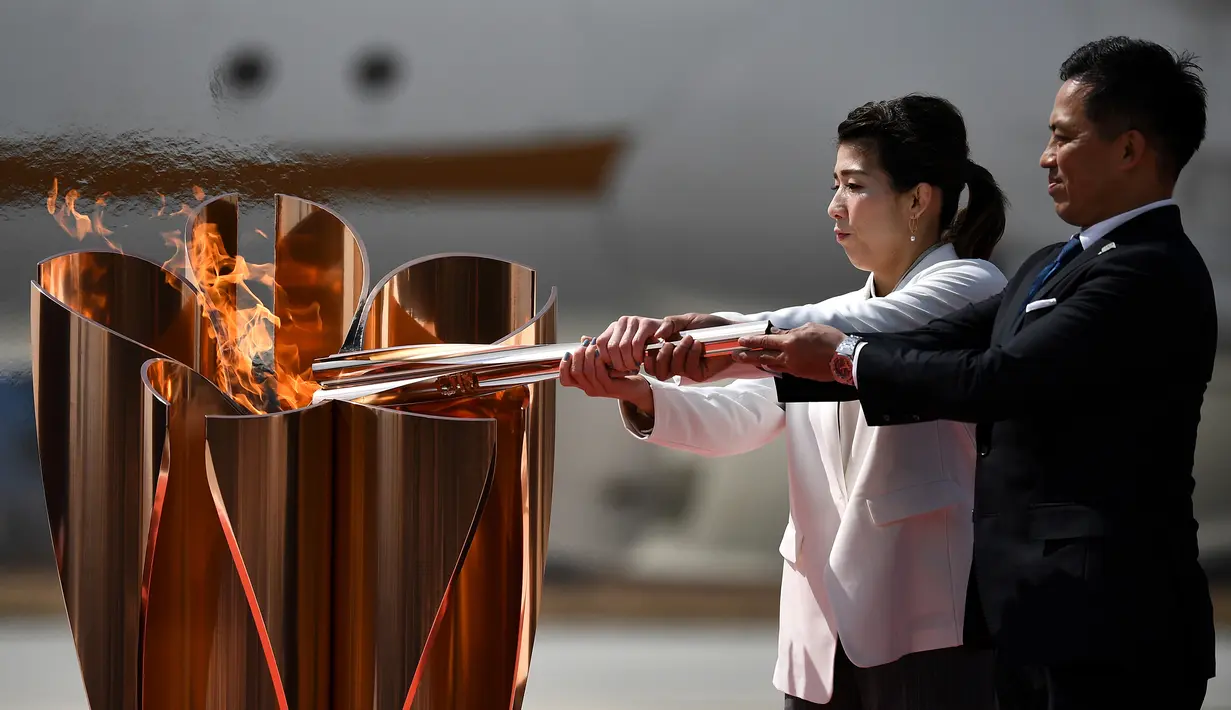 Atlet peraih tiga kali medali emas olimpiade, Tadahiro Nomura dan Saori Yoshida, menyalakan obor Olimpiade saat tiba dari Yunani di Pangkalan Udara Matsushima, Jepang, Jumat (20/3). Prosesi menuju Olimpiade Tokyo 2020 masih terus berjalan.(AFP/Philip Fong)
