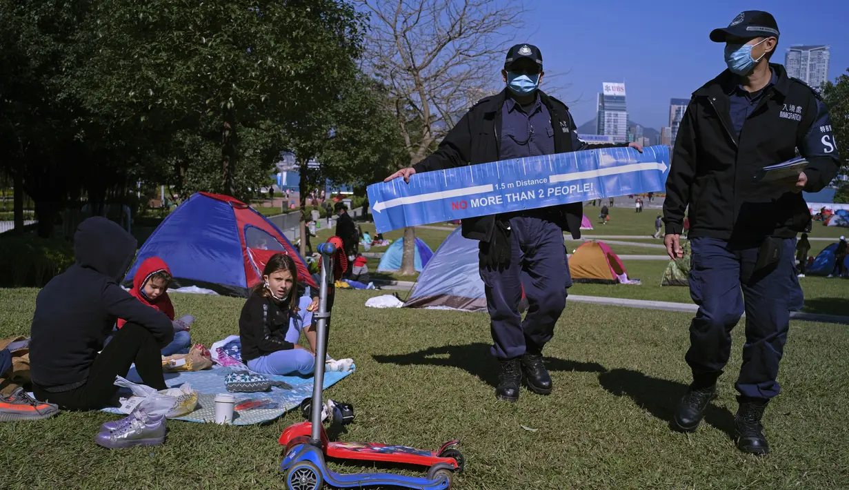 Petugas polisi membawa spanduk yang menunjukkan jarak sosial untuk mencegah penyebaran virus corona kepada pengunjung di taman di Hong Kong (2/1/2021). Hong Kong telah memesan 7,5 juta dosis vaksin China Sinovac Biotech Ltd dan 7,5 juta dosis Fosun Pharma- BioNTech. (AP Photo/Vincent Yu)