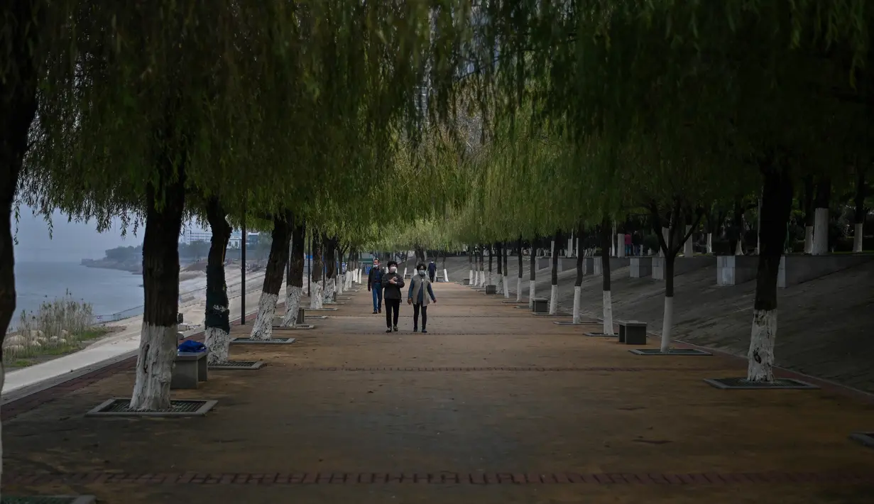 Orang-orang yang memakai masker wajah berjalan di taman di sebelah Sungai Yangtze di Wuhan (20/11/2020). Beberapa warga sudah tidak menggunakan masker saat melakukan aktivitas di luar ruangan. (AFP/Hector Retamal)
