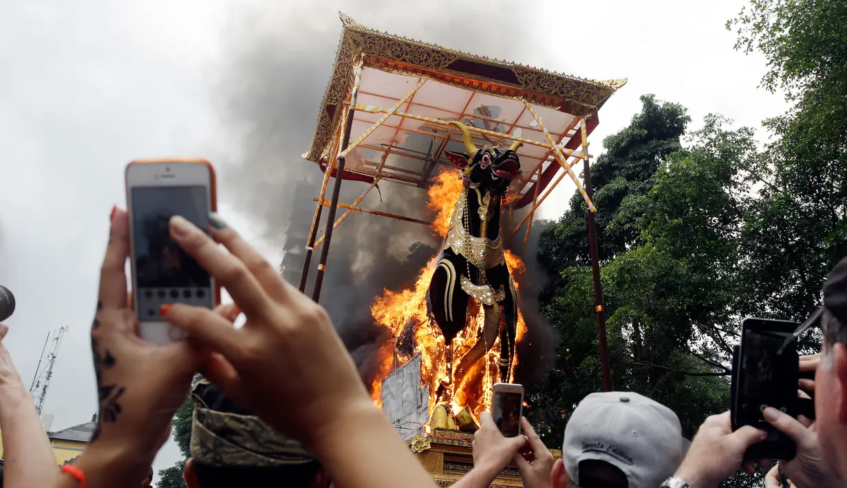 Wisatawan mengambil gambar  bade yang berisi tubuh Anak Agung Niang Agung terbakar saat ngaben keluarga Kerajaan Puri Ubud di Bali, Indonesia, Jumat (2/3). Anak Agung Niang Agung meninggal dunia Januari lalu di usia 96 tahun. (AP Photo/Firdia Lisnawati)