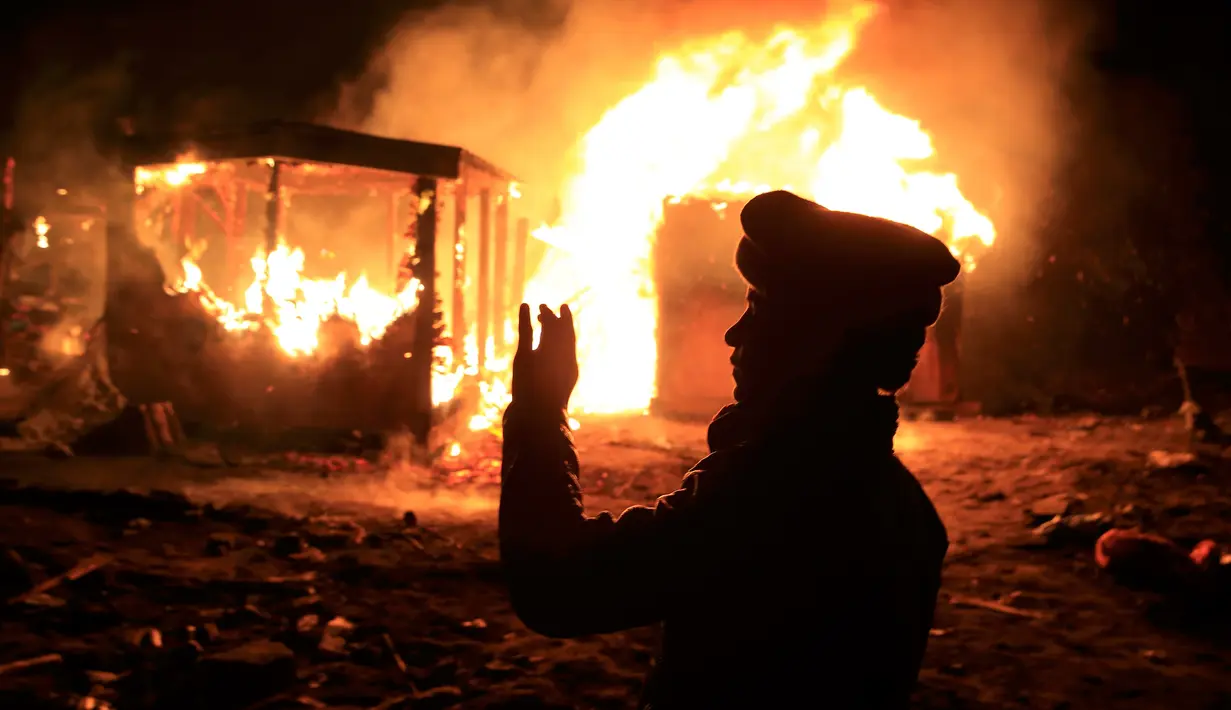 Imigran berdiri di depan tempat tinggalnya yang dibakar pihak berwenang di lahan kumuh yang dijuluki "Jungle" di Calais, Prancis (1/3). Pembakaran ini memunculkan protes bagi ribuan imigran yang tinggal di lokasi tersebut. (REUTERS/Pascal Rossignol)