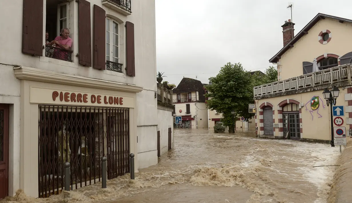 Seorang pria berada di jendela lantai pertama menyaksikan banjir merendam jalanan setelah hujan lebat di Salies-de-Bearn, Perancis barat daya (13/6). (AFP Photo/Iroz Gaizka)