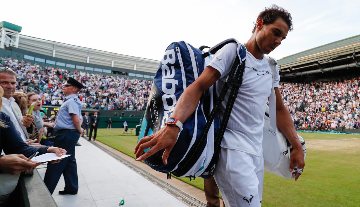 Petenis Spanyol, Rafael Nadal memberikan tanda tangan sambil meninggalkan lapangan usai kalah dari Giller Muller (Luksemburg) di perempat final Wimbledon 2017, Senin (10/7). Nadal kalah dengan skor akhir 3-6, 4-6, 6-3, 6-4, 13-15. (Adrian DENNIS/AFP)